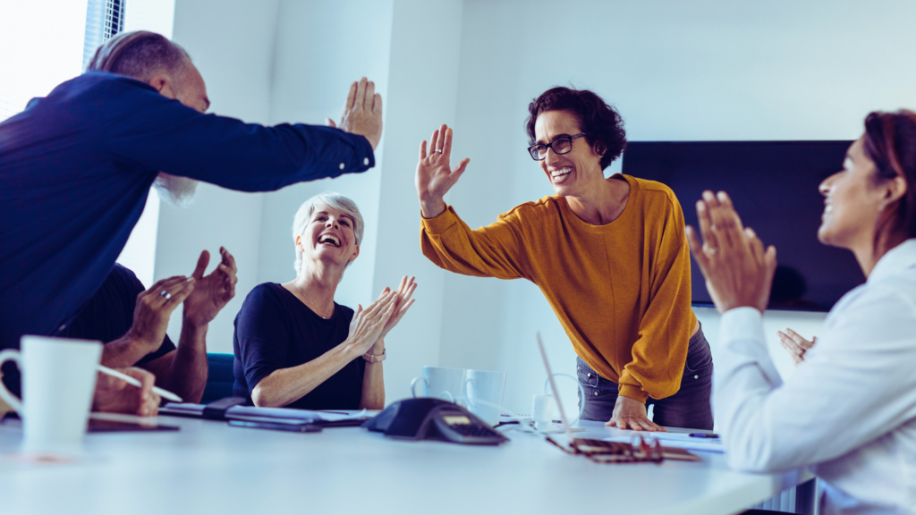 Menschen sitzen in einem Meeting und klatschen sich ab, während sie gemeinsam Erfolg feiern