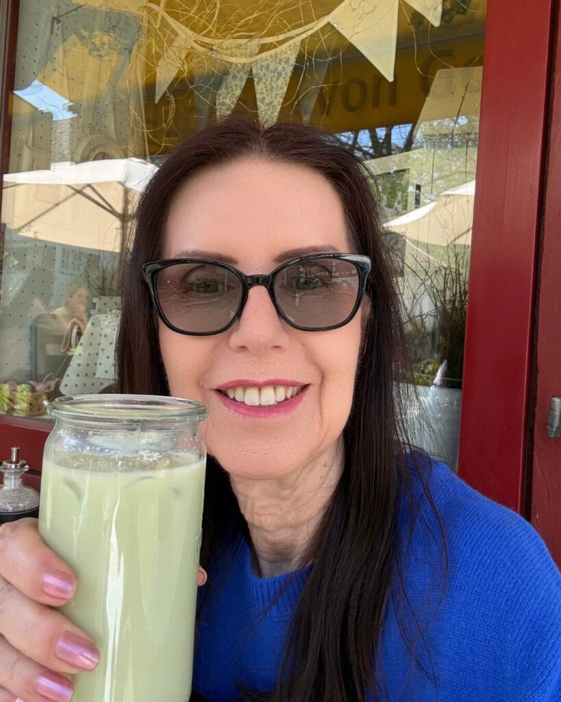 Gabriele Danners hält ein Glas Matcha Latte und sitzt entspannt in einem Café