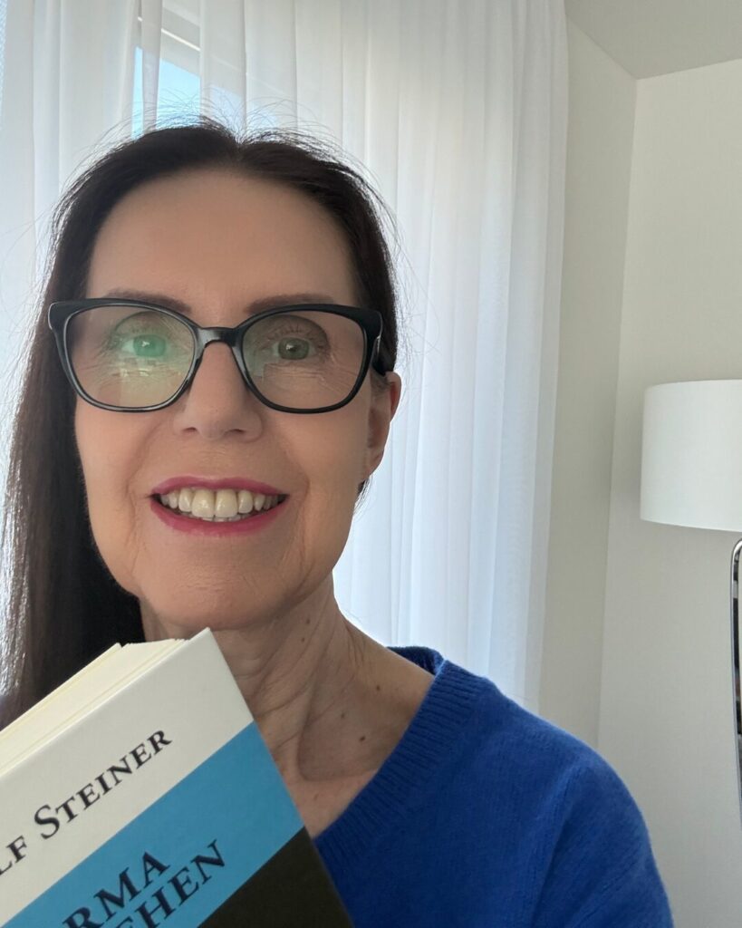 Gabriele Danners lächelt und hält ein Buch in der Hand in einem hellen Raum mit Vorhängen