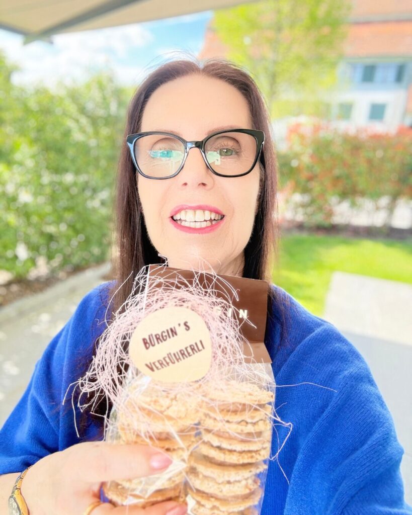 Gabriele Danners lächelt und hält eine Tüte mit Gebäck in der Hand in einem Garten
